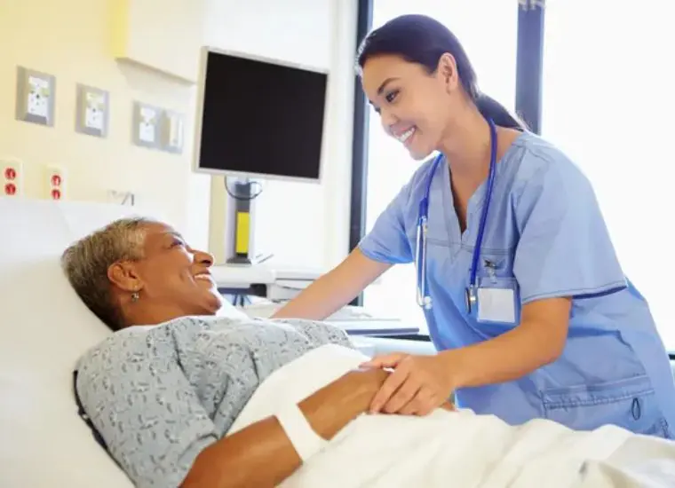 A nurse is smiling at an older patient in the hospital.