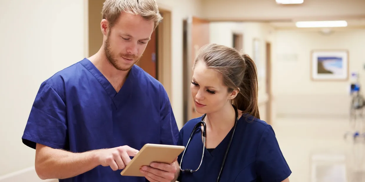 A man and woman in scrubs looking at an ipad.