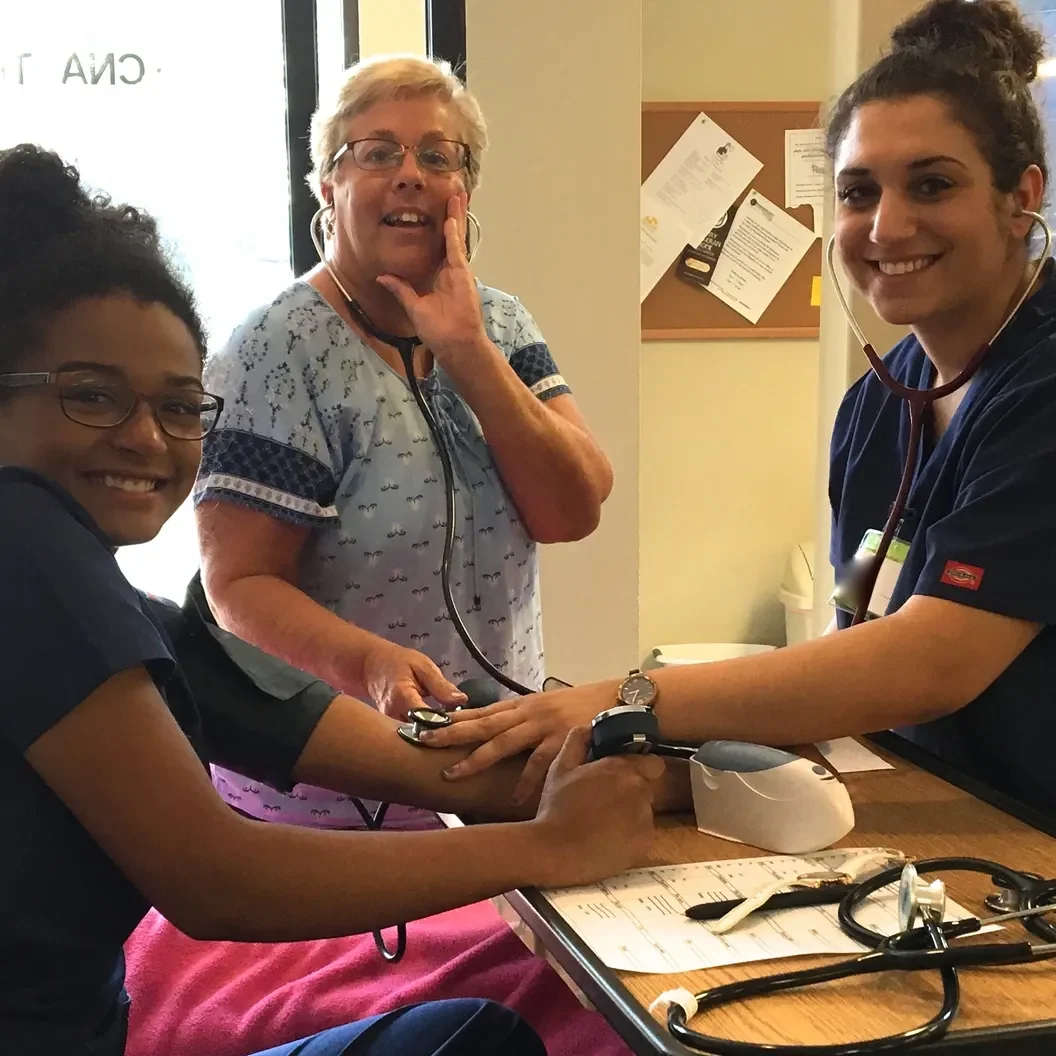 Three nurses are smiling while one of them is holding a phone.